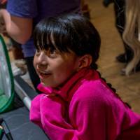 indoor photo at eye-level with a young girl, seven years old or so, leaning on a table in a sweatshirt and looking up